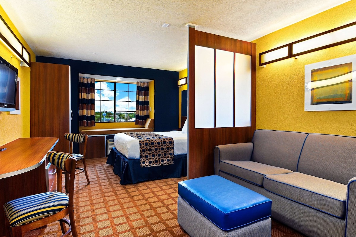 A hotel room with a bed, a sofa, a dining table with chairs, a TV, and a window with curtains.