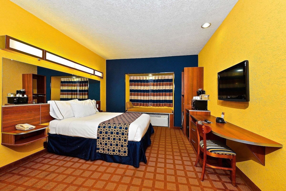 A hotel room with a bed, a desk, a chair, a television, and a window with curtains.