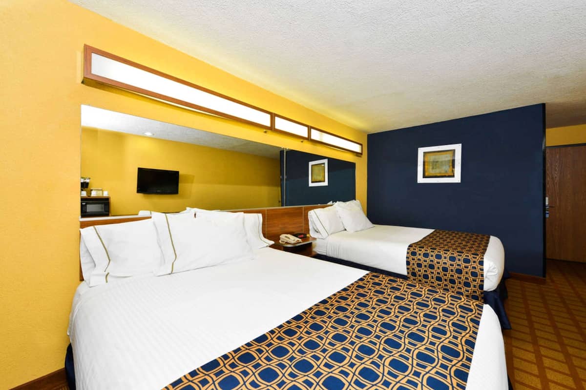 A hotel room with two beds, a television, a desk, and a mirror.
