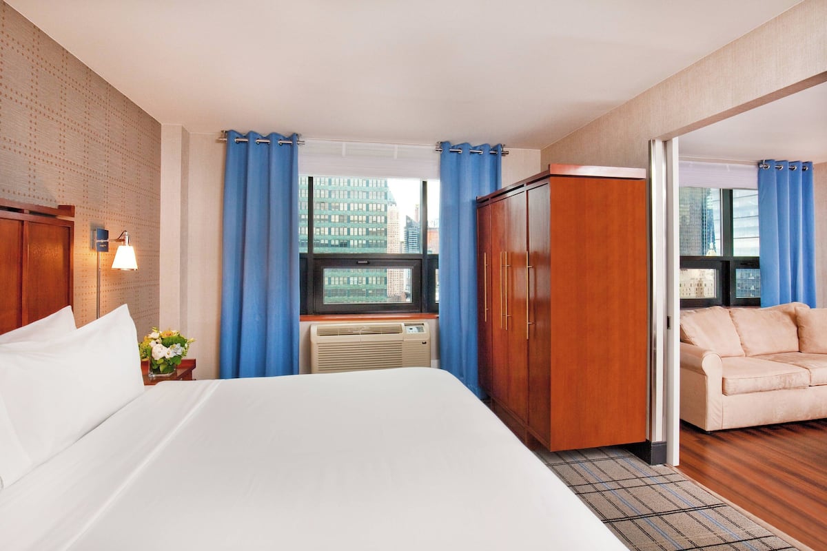 A hotel room with a large bed, a wooden wardrobe, a sofa, and a window with curtains.
