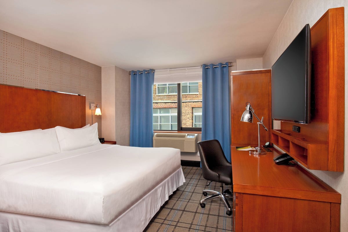 A hotel room with a large bed, a desk with a television, a chair, and a window with curtains.