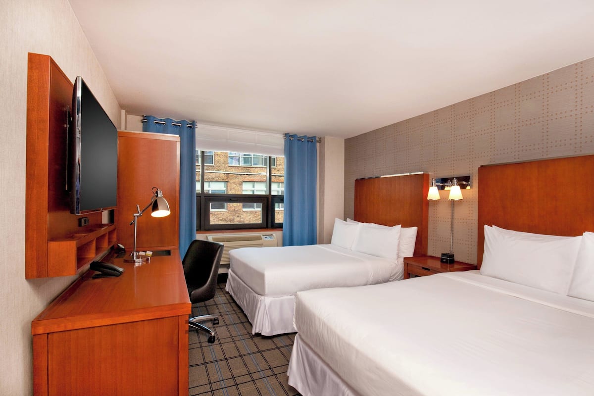 A hotel room with two beds, a desk, a chair, a TV, and a window with curtains.