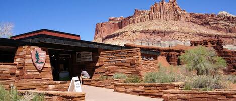 A visitor center with a stone facade, a sign for the Geology Program, and a backdrop of red rock formations.