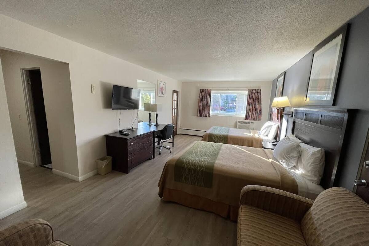 A hotel room with two beds, a desk with a chair, a TV, and a window with curtains.