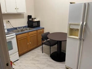 A compact kitchen with a stove, microwave, sink, and a small dining table with two chairs. - Village Inn (Green Bay)