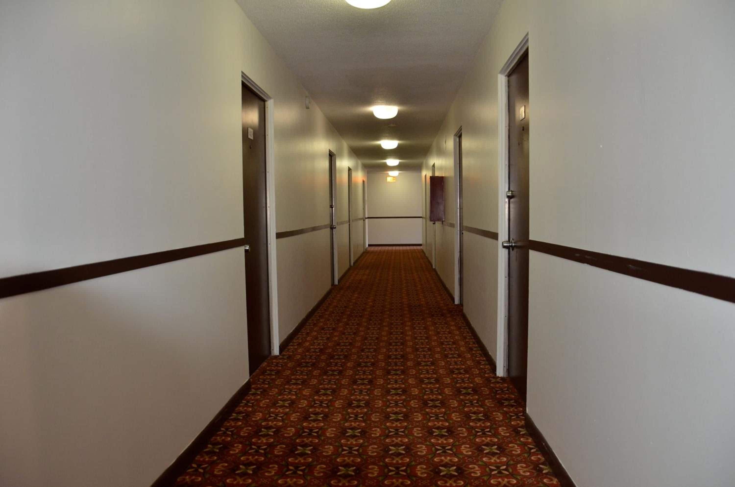 A long, narrow hotel corridor with carpeted floors and doors on both sides.