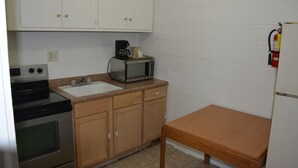 A compact kitchen with white cabinets, a microwave, a coffee maker, an oven, and a small wooden table.