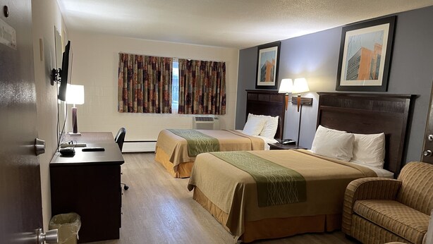 A hotel room with two beds, a desk, a chair, a trash bin, and a wall-mounted air conditioner.