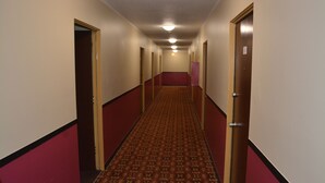 A hotel hallway with a patterned carpet, red walls, and doors leading to rooms.