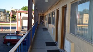 A building with a covered walkway, a parked car, and a person sitting on a bench.