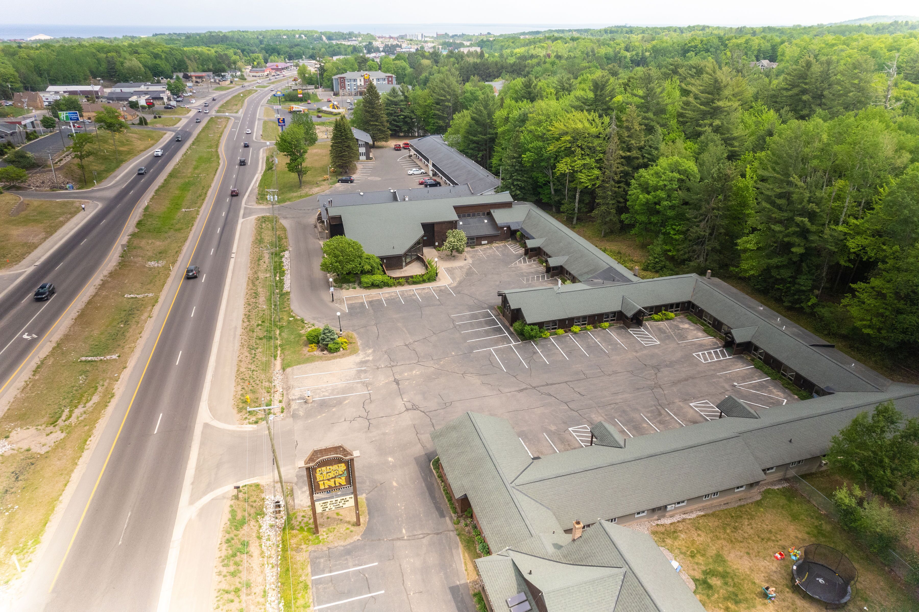 An aerial view of a hotel with a large parking lot, multiple buildings, and a road with vehicles.