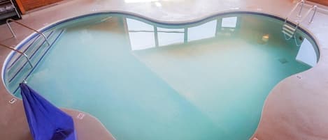 An indoor swimming pool with a wooden interior, clear water, and a blue towel on the left.