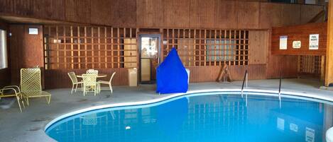 A pool area with a wooden deck, chairs, and a blue tent.