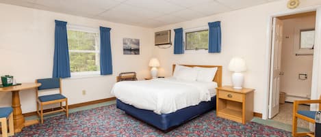 A hotel room with a bed, two bedside tables, a chair, a desk, a patterned carpet, and a window with curtains.