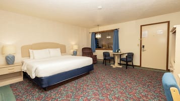 Quarto de hotel com uma cama, duas cadeiras, uma mesa pequena e uma janela com cortinas.