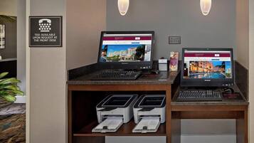 Balcão de recepção com dois laptops, uma impressora e um aviso indicando disponibilidade de TDD.