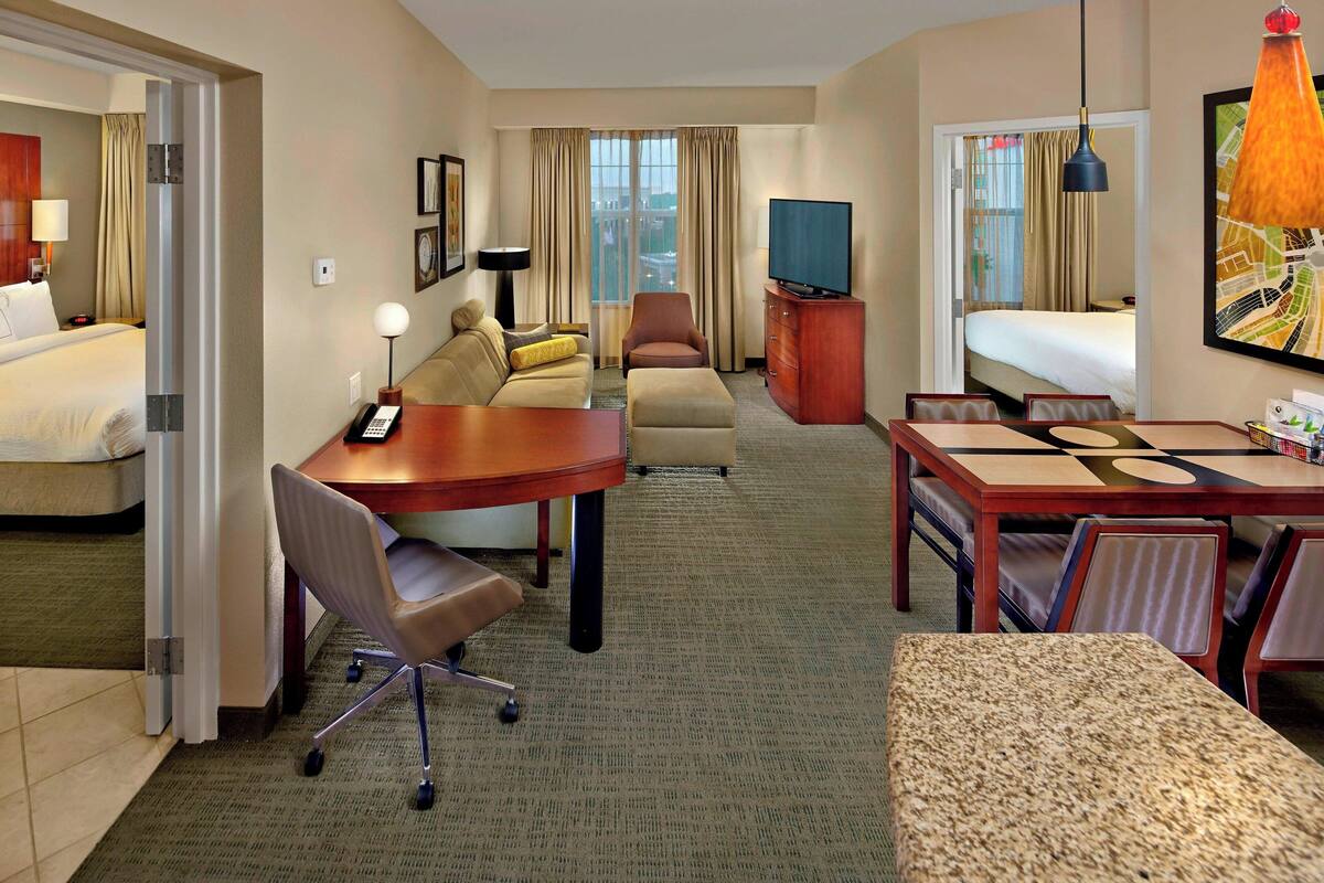 Une chambre d’hôtel comprenant un lit, un canapé, un bureau avec une chaise, une télévision et une table à manger avec des chaises.