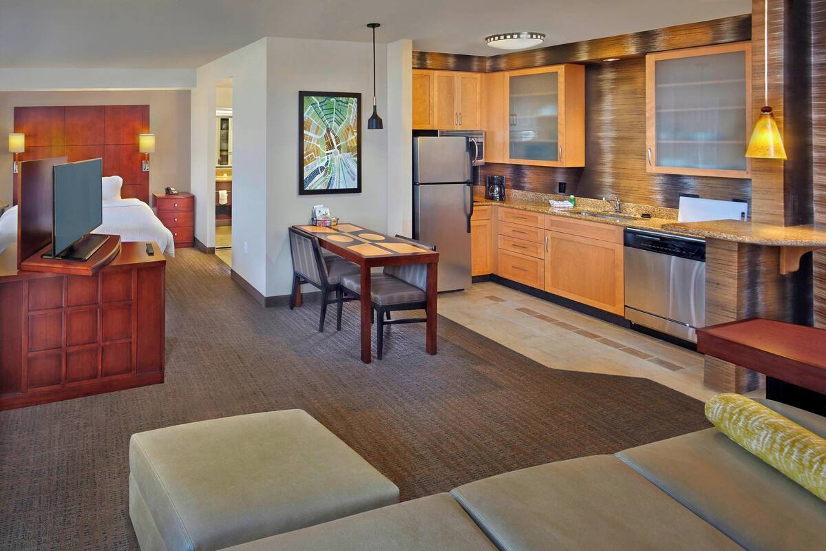 Une chambre d’hôtel moderne dotée d’une kitchenette, d’un coin repas et d’un espace salon avec un canapé et des fauteuils.