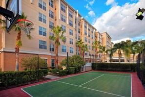 An outdoor tennis court adjacent to a multi-story hotel with palm trees and a basketball hoop. - Residence Inn by Marriott Orlando Lake Mary (Lake Mary)