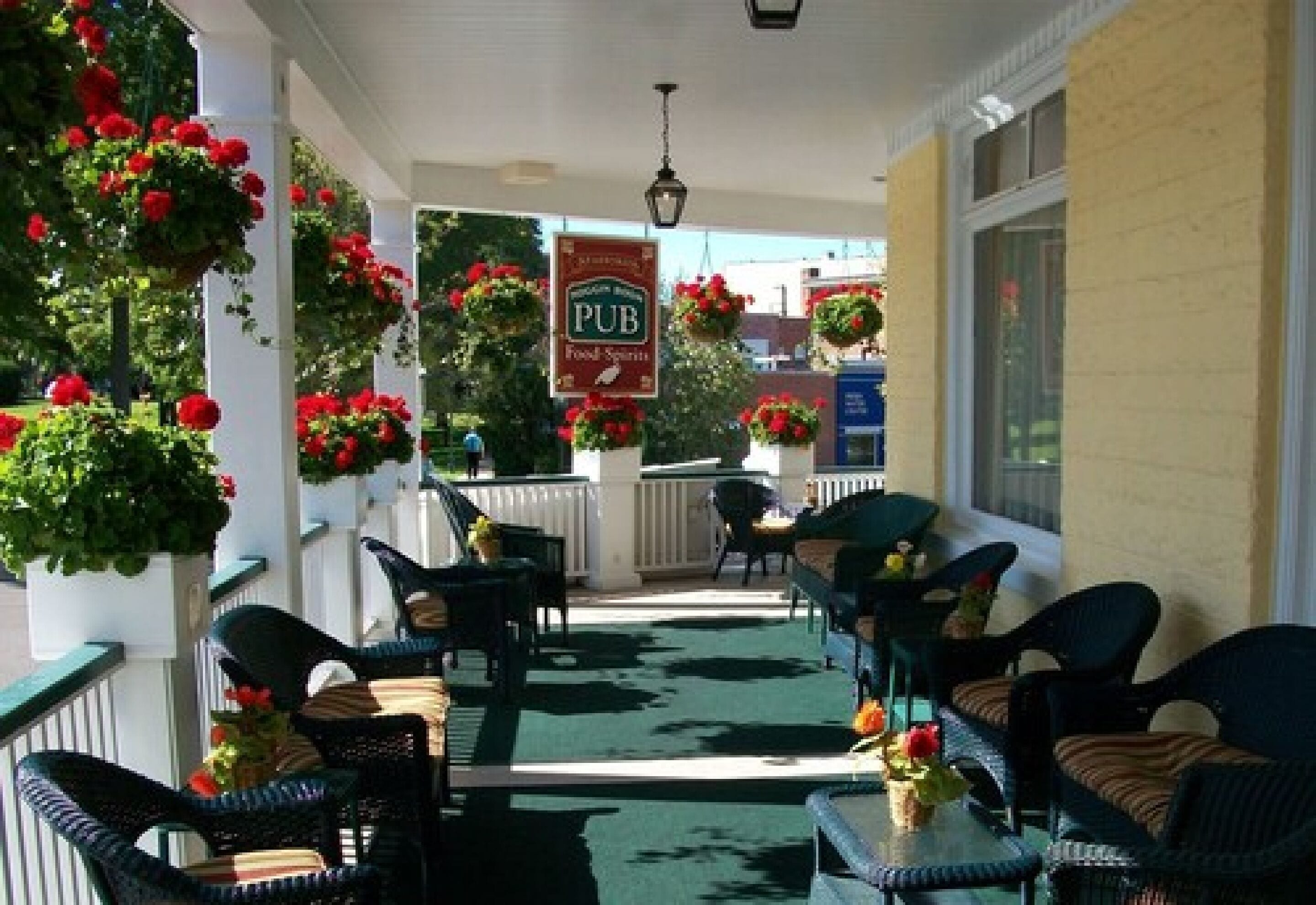 A covered outdoor seating area with wicker chairs and tables, potted plants, and a sign for a pub.