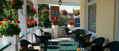 A covered outdoor seating area with wicker chairs and tables, potted plants, and a sign for a pub.