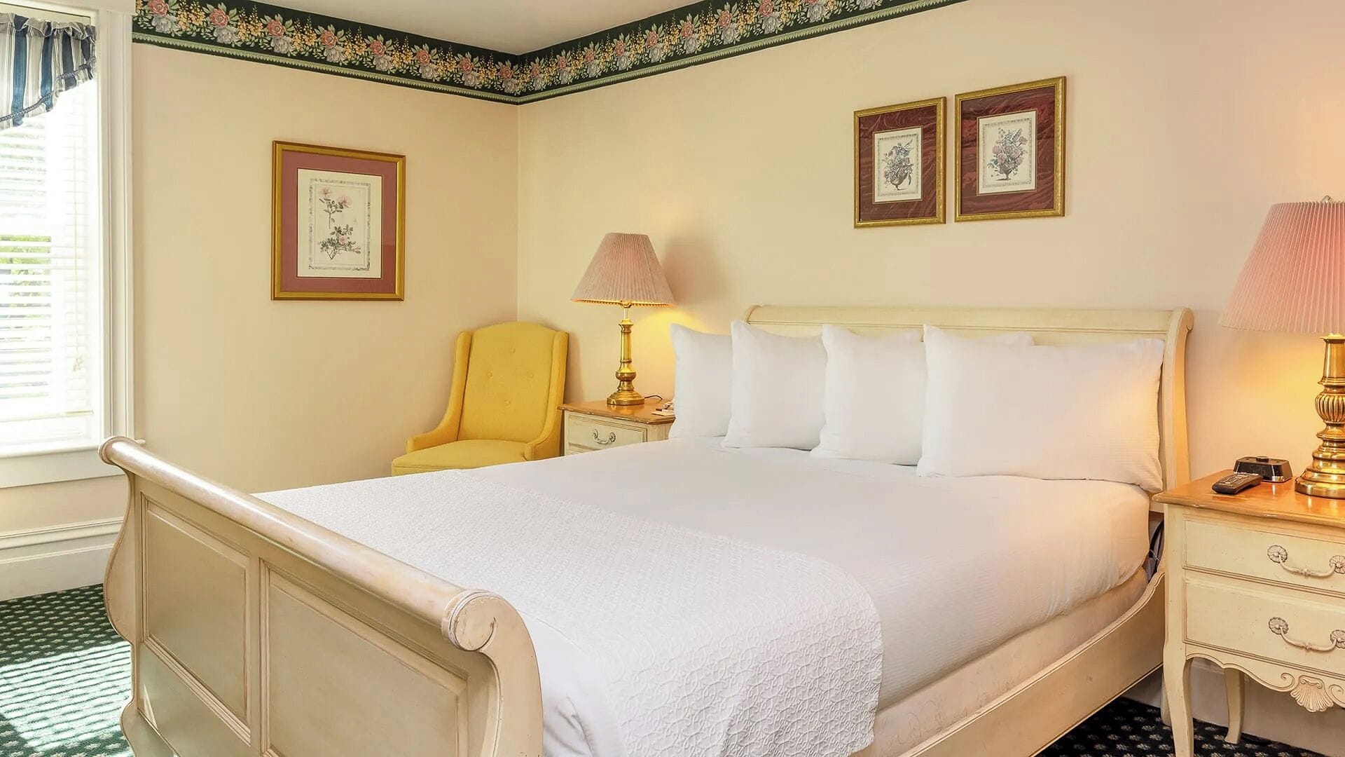 A hotel room with a bed, bedside tables, a chair, and framed pictures on the wall.