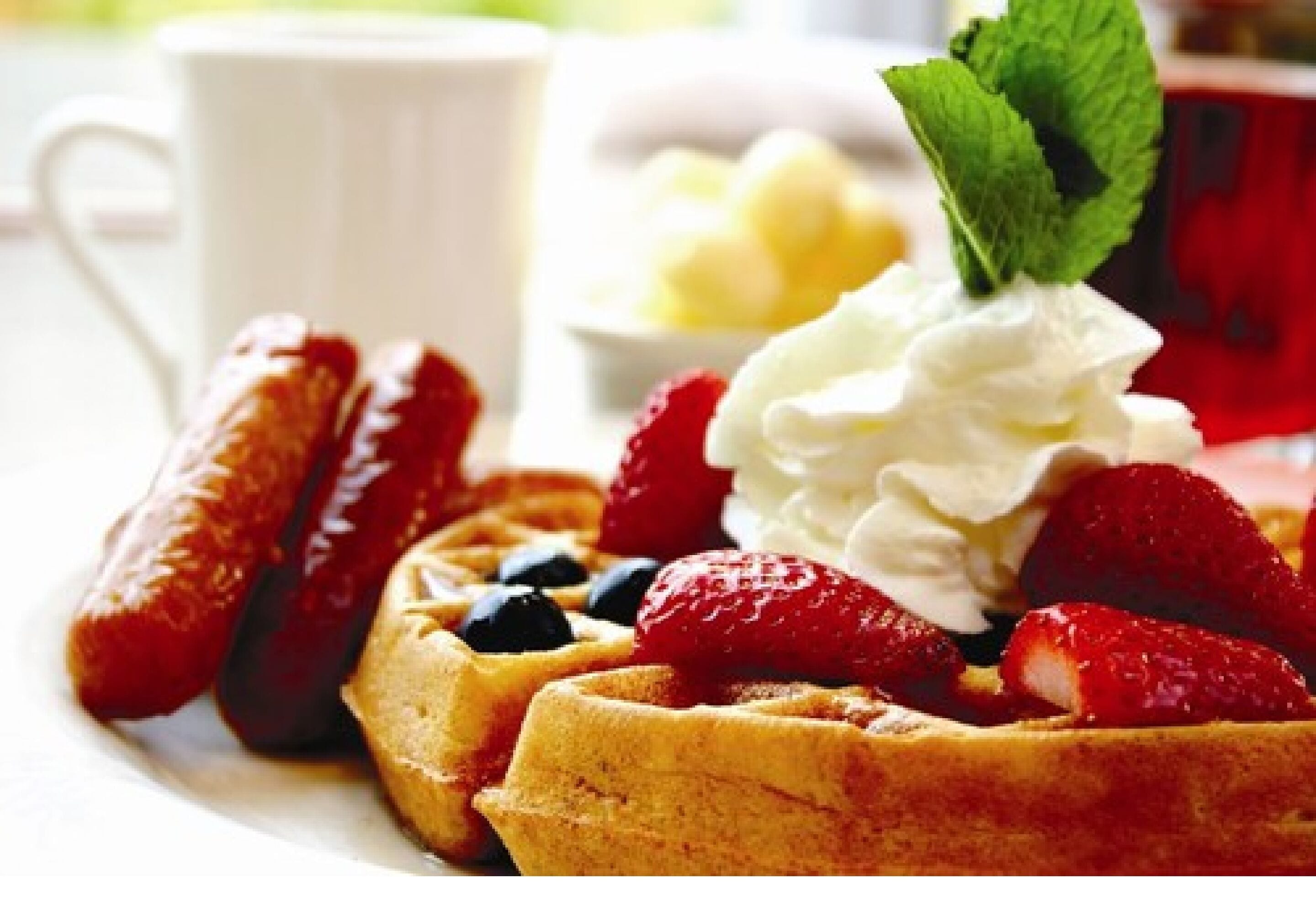 Une assiette de gaufres garnie de fraises, de myrtilles, de crème fouettée et d’une feuille de menthe.