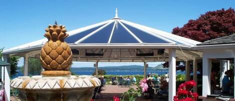 A gazebo with a pineapple-shaped fountain, surrounded by red flowers and a view of the sea.