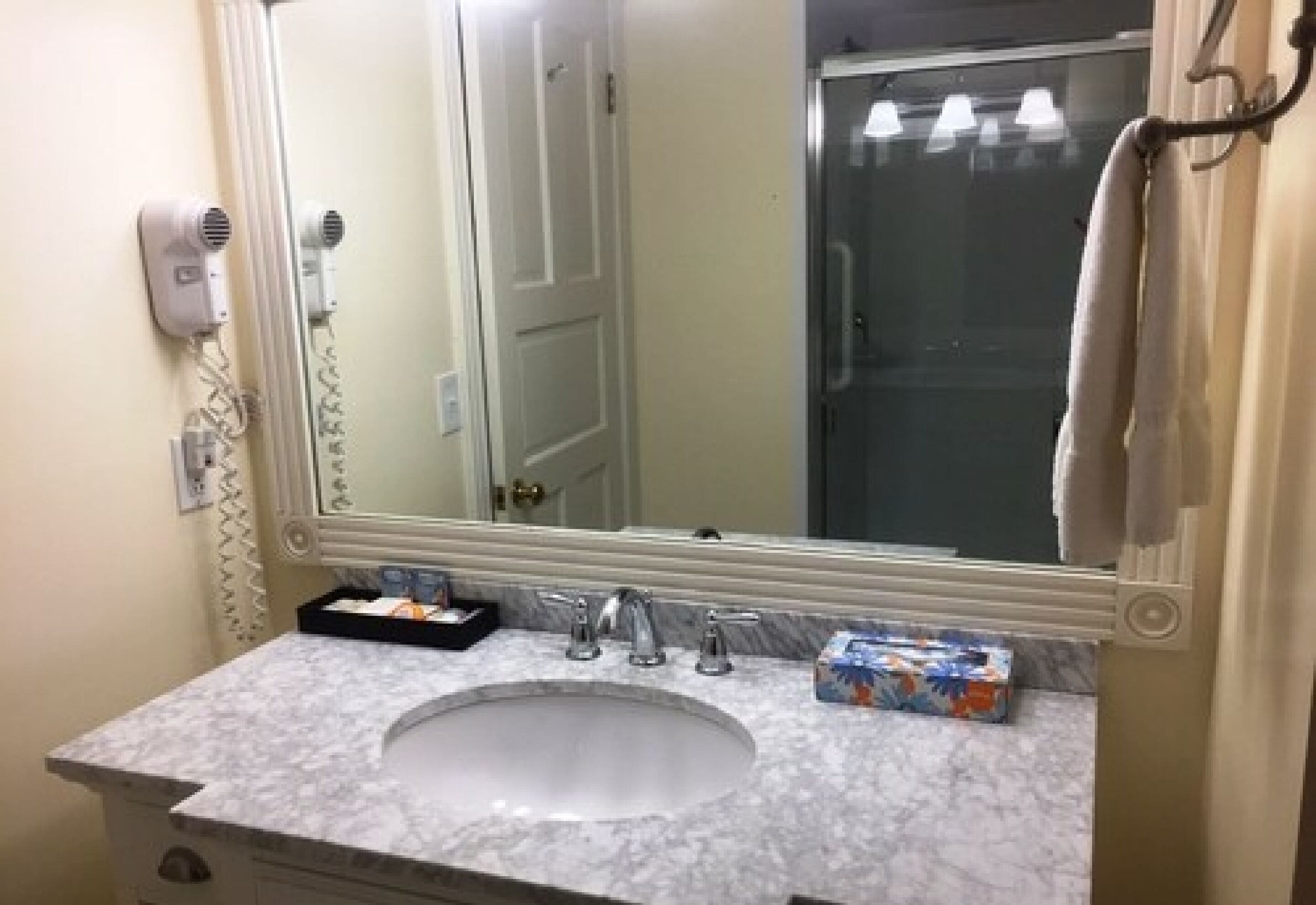 Un bagno con uno specchio grande, un lavandino, un asciugacapelli e un portasciugamani.
