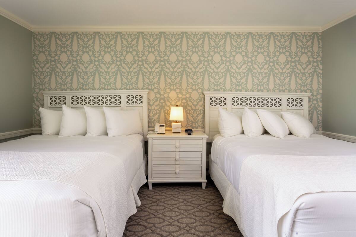 A twin room with two beds, a nightstand with a lamp, and patterned wallpaper.