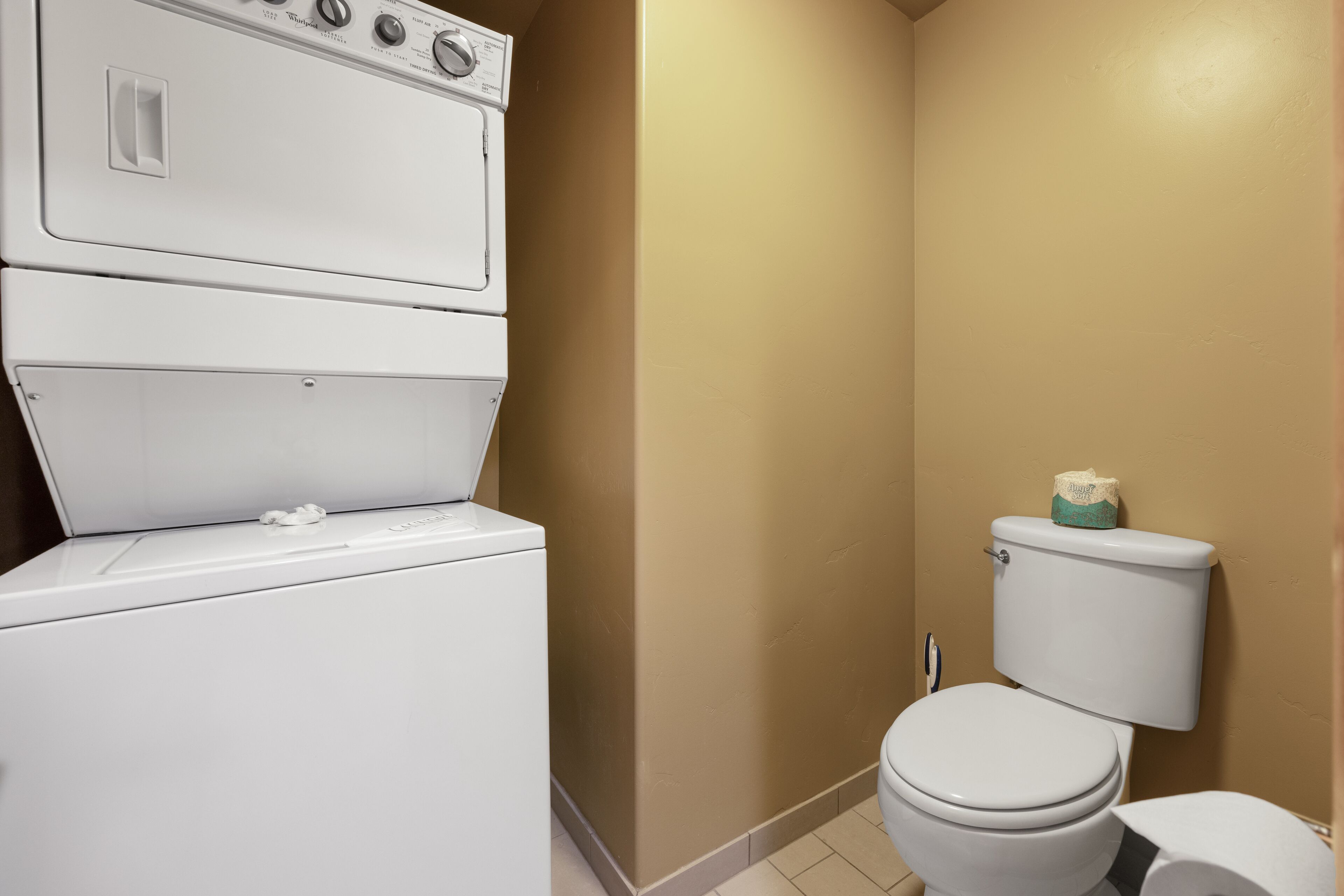 Baño pequeño con lavadora y secadora apiladas, un inodoro y una pared color crema.