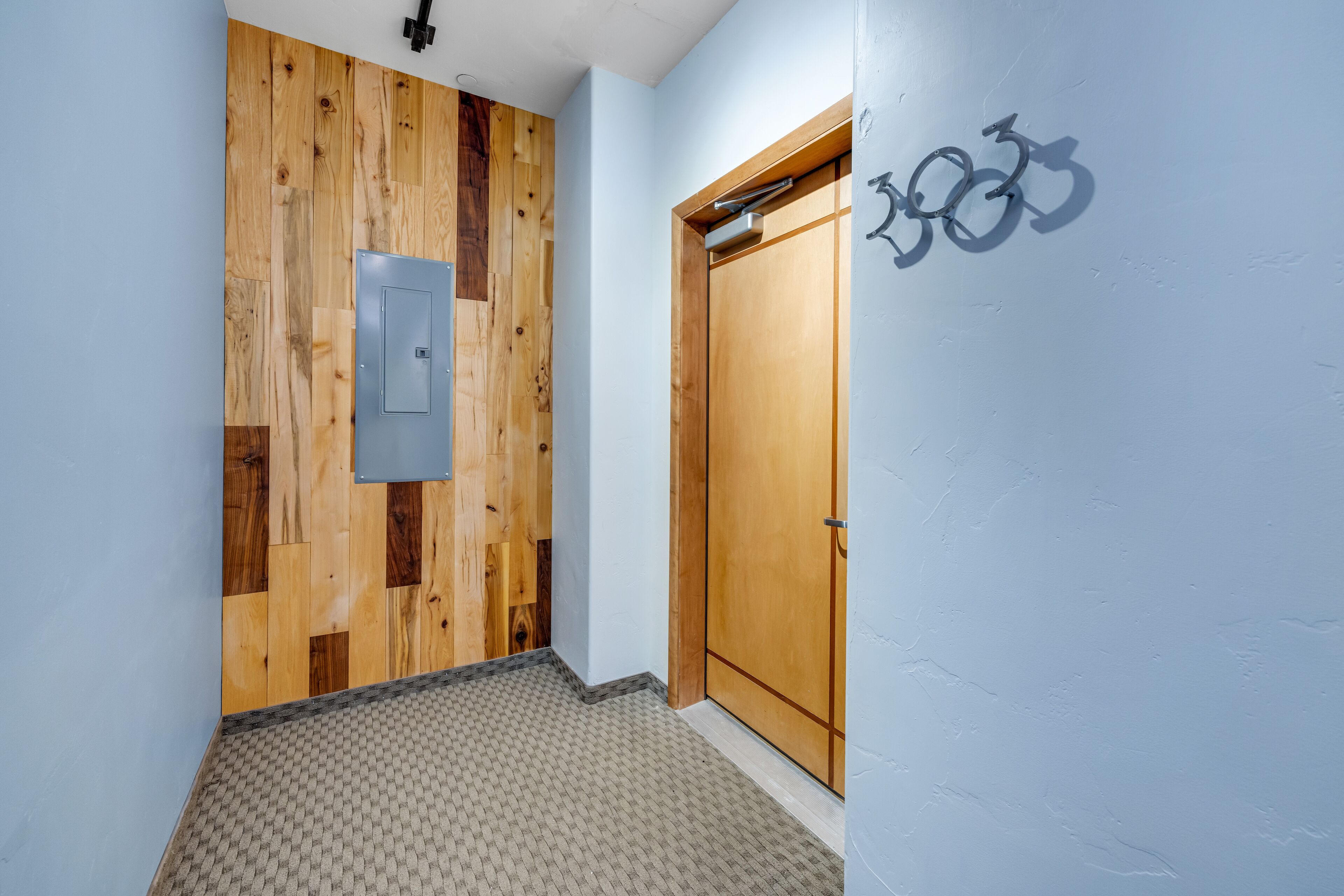 Ein Korridor mit einer Holzwand, einer Tür mit Fahrradsymbol und einem strukturierten Teppich.