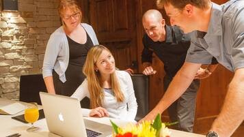 A group of people around a table with a laptop, a glass of orange juice, and a bouquet of flowers.