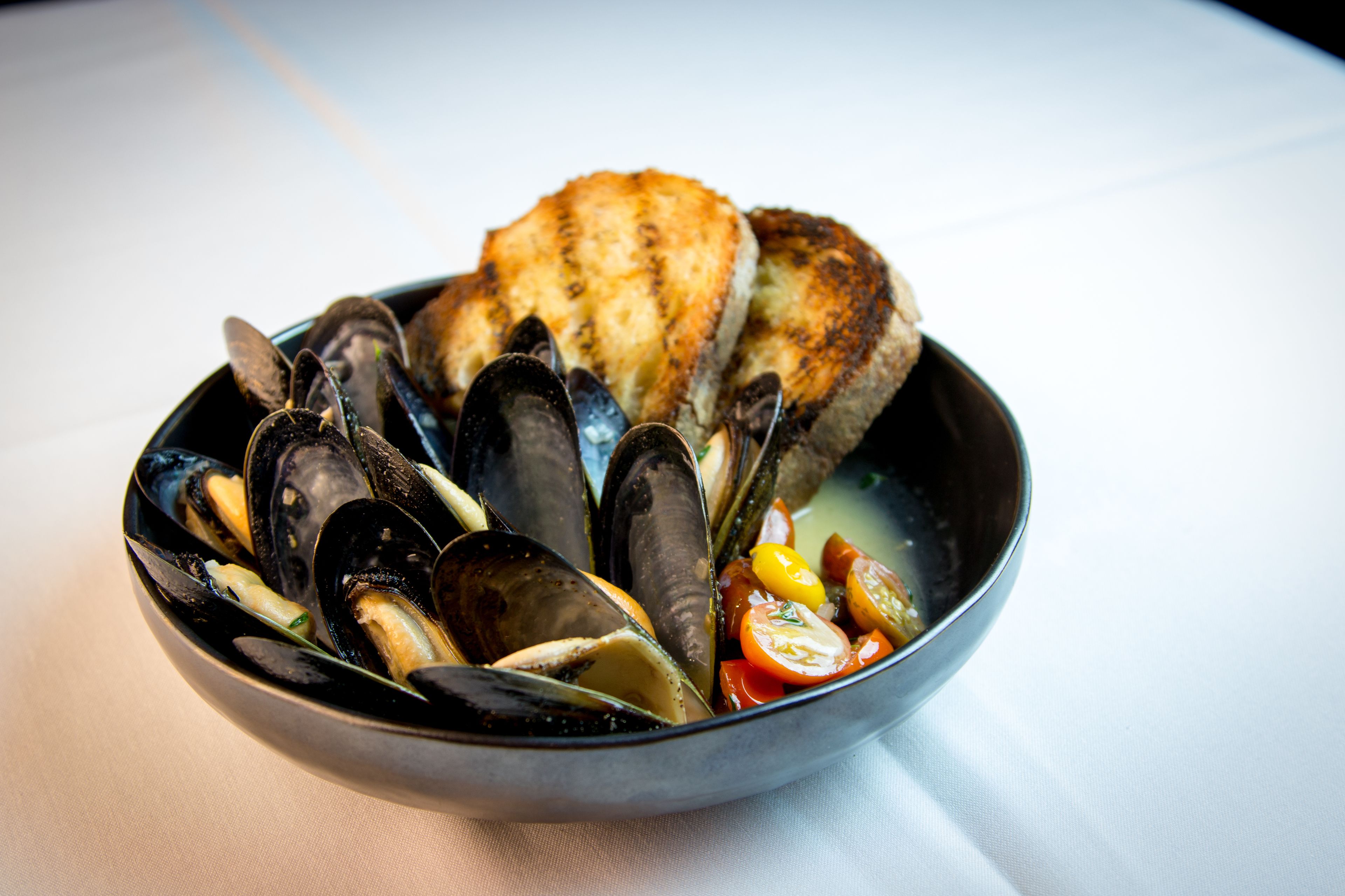 Eine Schale mit Muscheln, Brot und Tomaten.