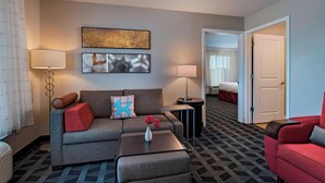 Habitación de hotel con un sofá gris, un sillón rojo, una mesita con un jarrón de flores y una alfombra estampada.