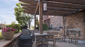 Un patio exterior con chimenea de piedra, una parrilla y una pérgola de madera.
