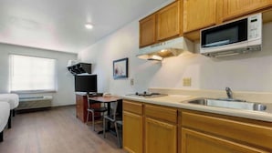A compact kitchen with wooden cabinets, a microwave, a sink, and a small dining area with a chair and table. - Studio 6 Extended Stay El Paso East TX (El Paso)