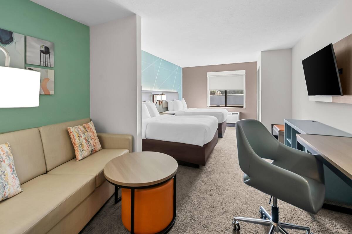 Ett hotellrum med en soffa, två sängar, ett skrivbord, en stol och en TV.