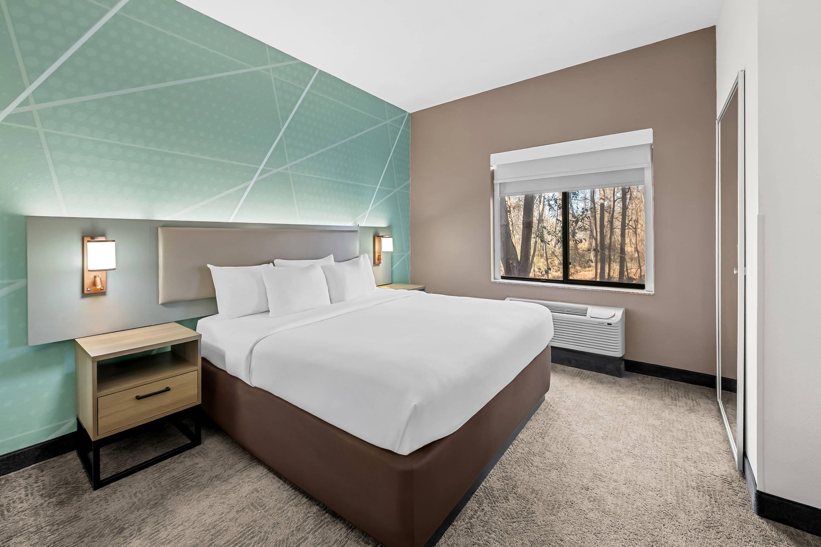 Una habitación de hotel con cama, mesita de noche, lámpara, ventana y decoración en la pared.
