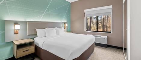A hotel room with a bed, bedside table, lamp, window, and wall decor.