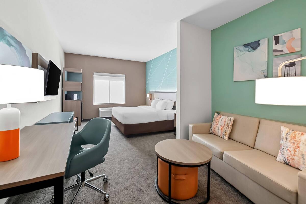 Ett hotellrum med en säng, ett skrivbord, en stol, en soffa, ett runt bord och konstverk på väggarna.
