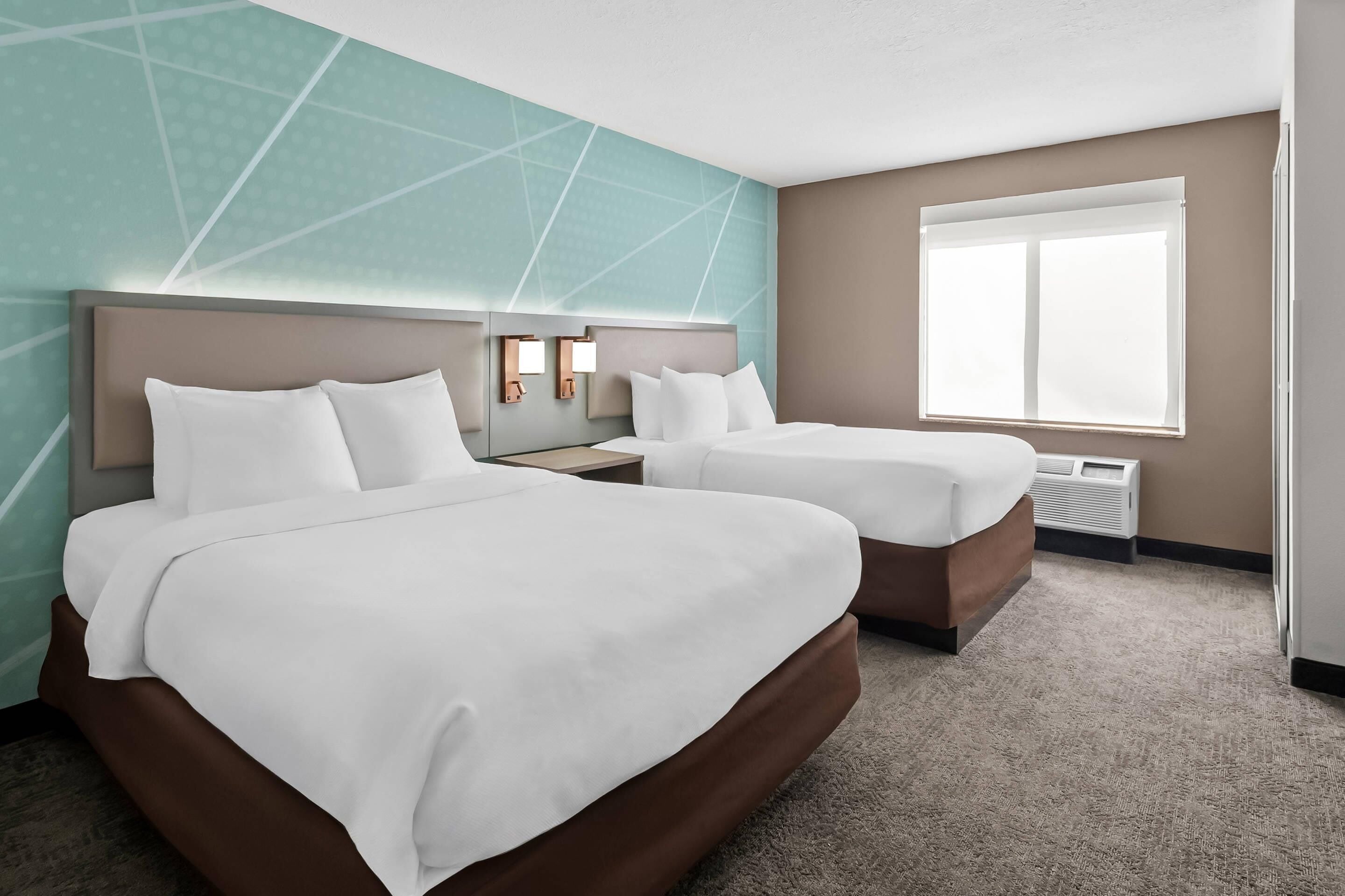 A hotel room with two beds, a large window, and a wall with geometric patterns.