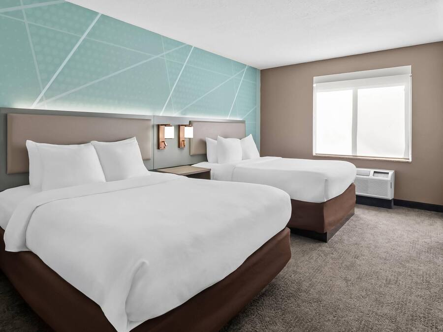 A hotel room with two beds, a large window, and a wall with geometric patterns.