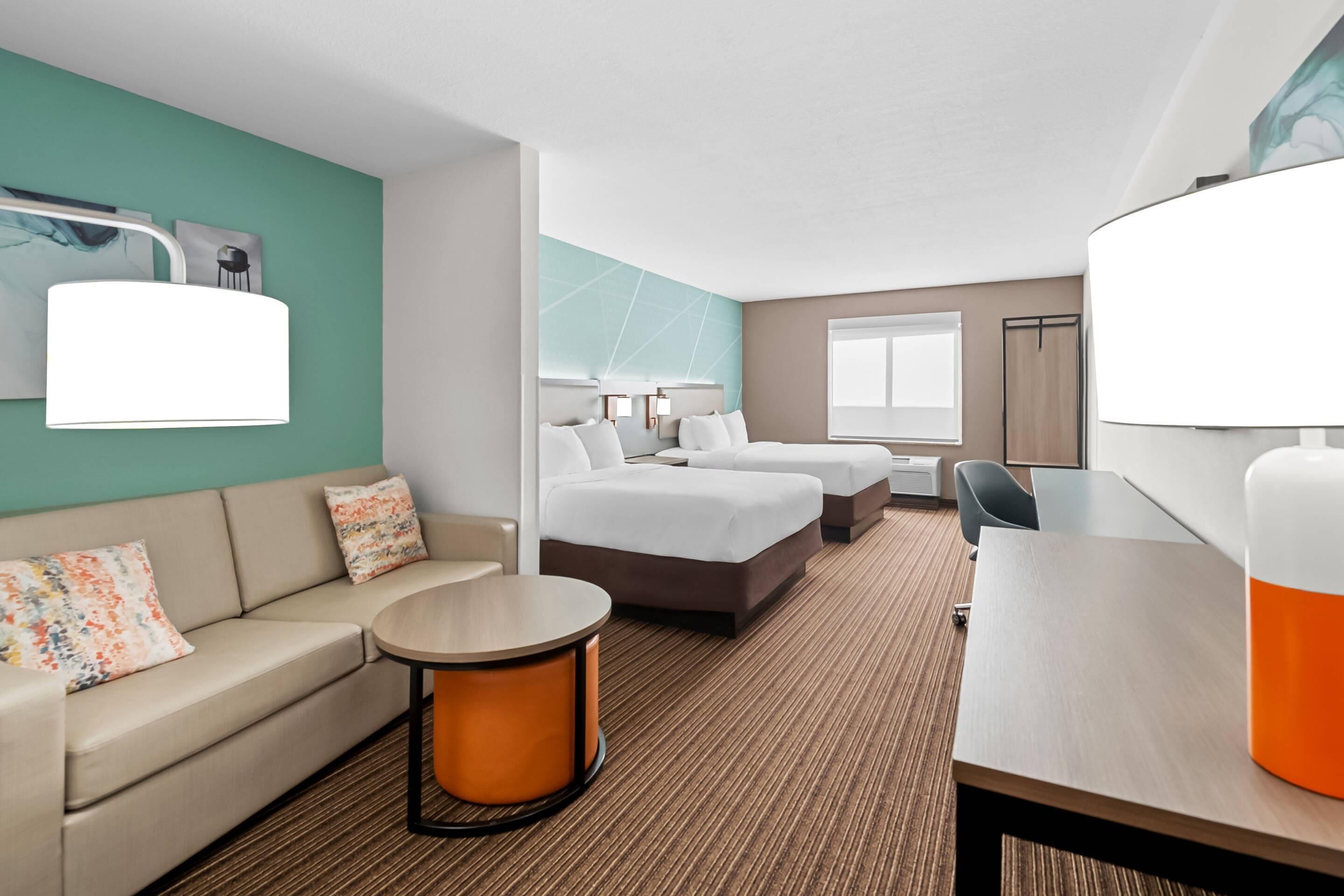 A hotel room with a sofa, two beds, a round table, and a desk.