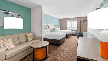 A hotel room with a sofa, two beds, a round table, and a desk.