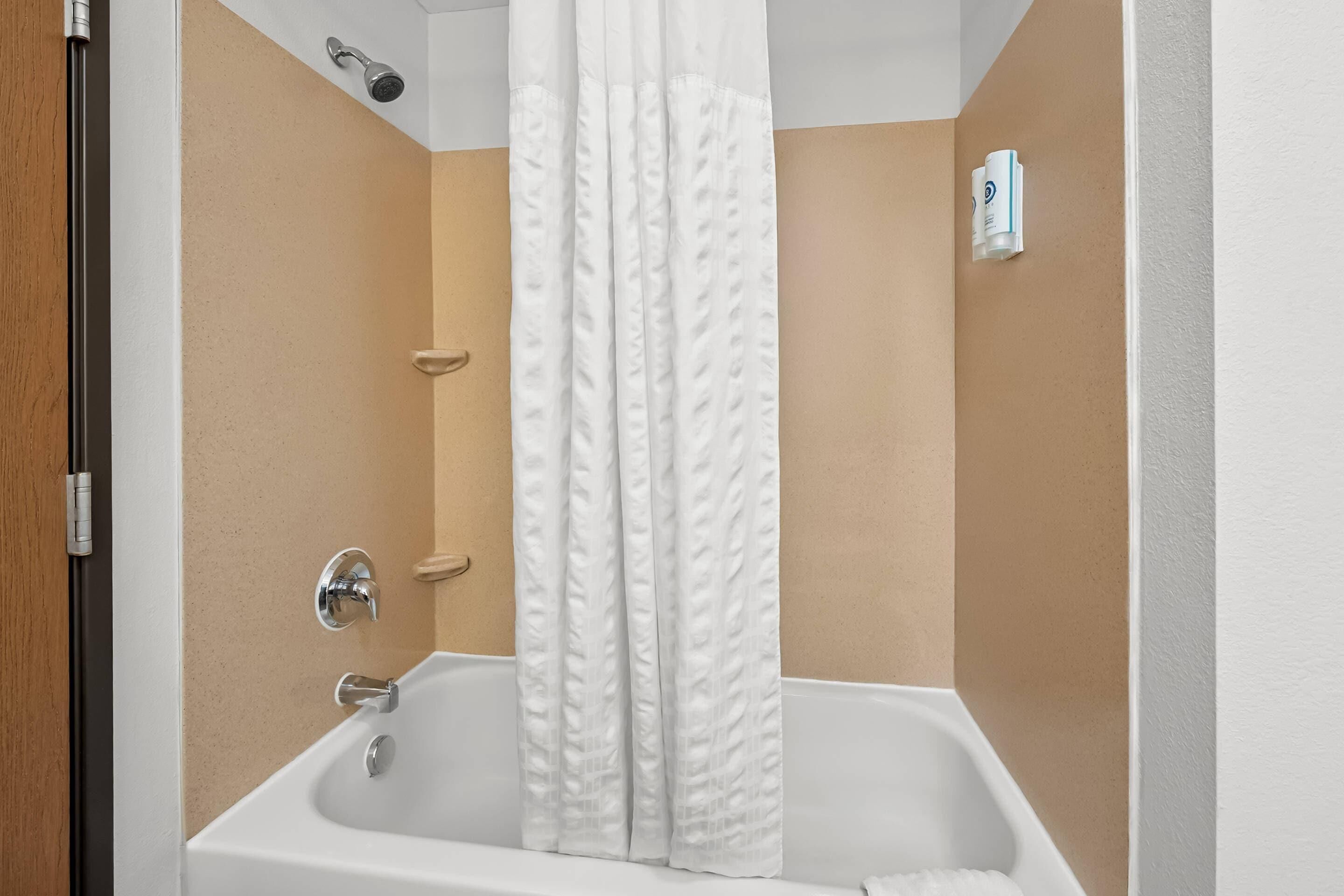A bathroom with a bathtub, shower curtain, and a wall-mounted towel dispenser.
