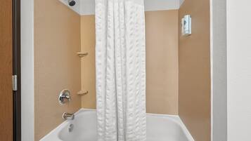 A bathroom with a bathtub, shower curtain, and a wall-mounted towel dispenser.