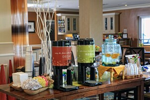 A buffet setup with coffee dispensers, a bowl of napkins, and a tray of fruits.