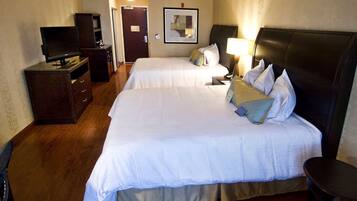 A hotel room with two beds, a TV, a desk, and a mirror.