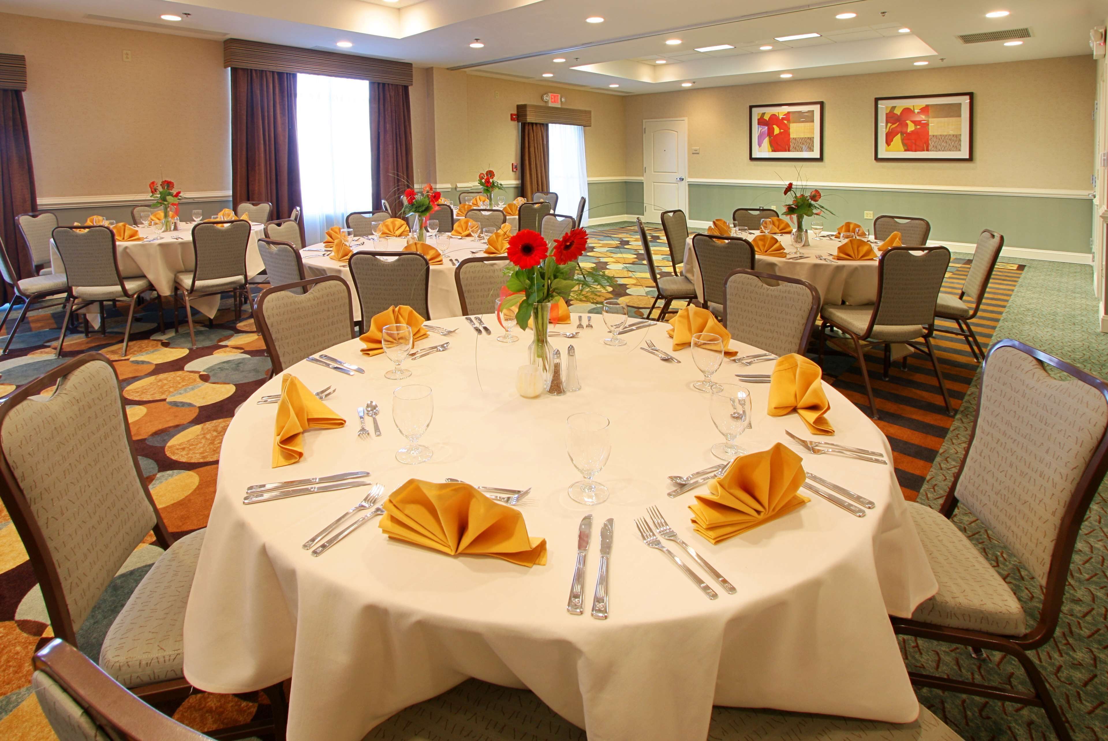 Un salón de conferencias con mesas redondas, sillas y un arreglo floral central.